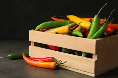 Photo of Wooden crate with different chili peppers on grey table