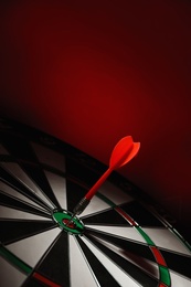 Photo of Color arrow hitting target on dart board against red background