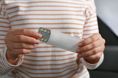 Photo of Woman holding blister with birth control pills indoors, closeup