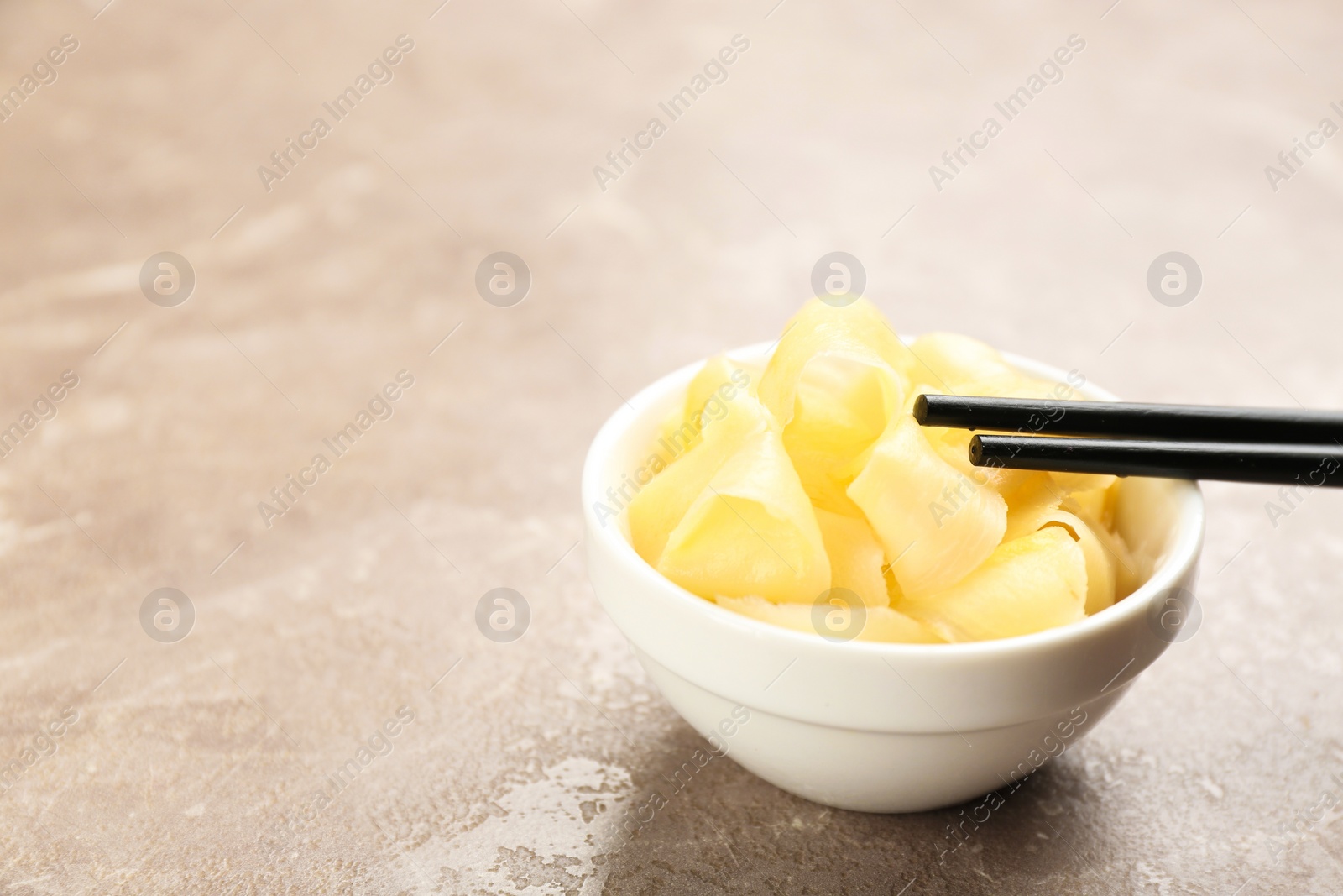 Photo of Spicy pickled ginger and chopsticks on grey table. Space for text