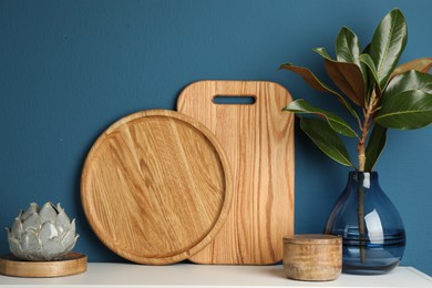 Photo of Wooden cutting boards, branch with green leaves and decor on white table near blue wall