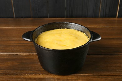 Photo of Fondue pot with melted cheese on wooden table