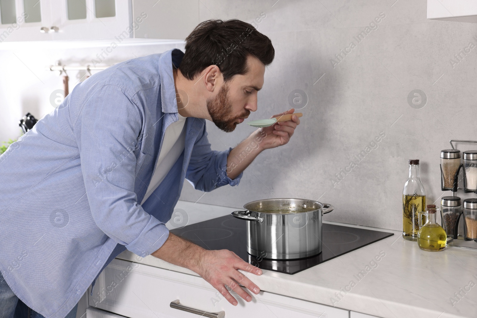 Photo of Man tasting delicious soup with spoon in kitchen