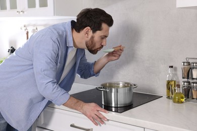 Man tasting delicious soup with spoon in kitchen