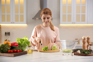 Photo of Young woman cooking at table in kitchen