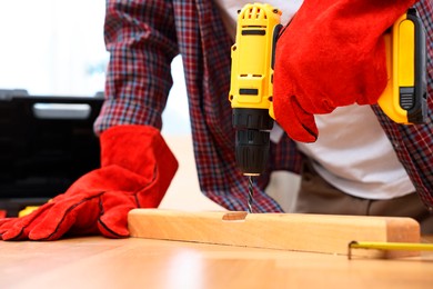 Photo of Young handyman working with electric drill at table in workshop, closeup