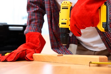 Young handyman working with electric drill at table in workshop, closeup