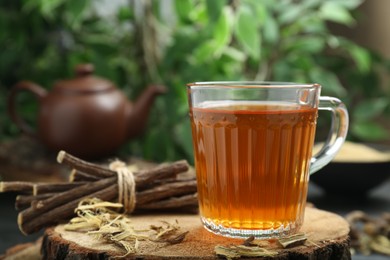 Photo of Aromatic licorice tea in cup and dried sticks of licorice root on table, closeup. Space for text