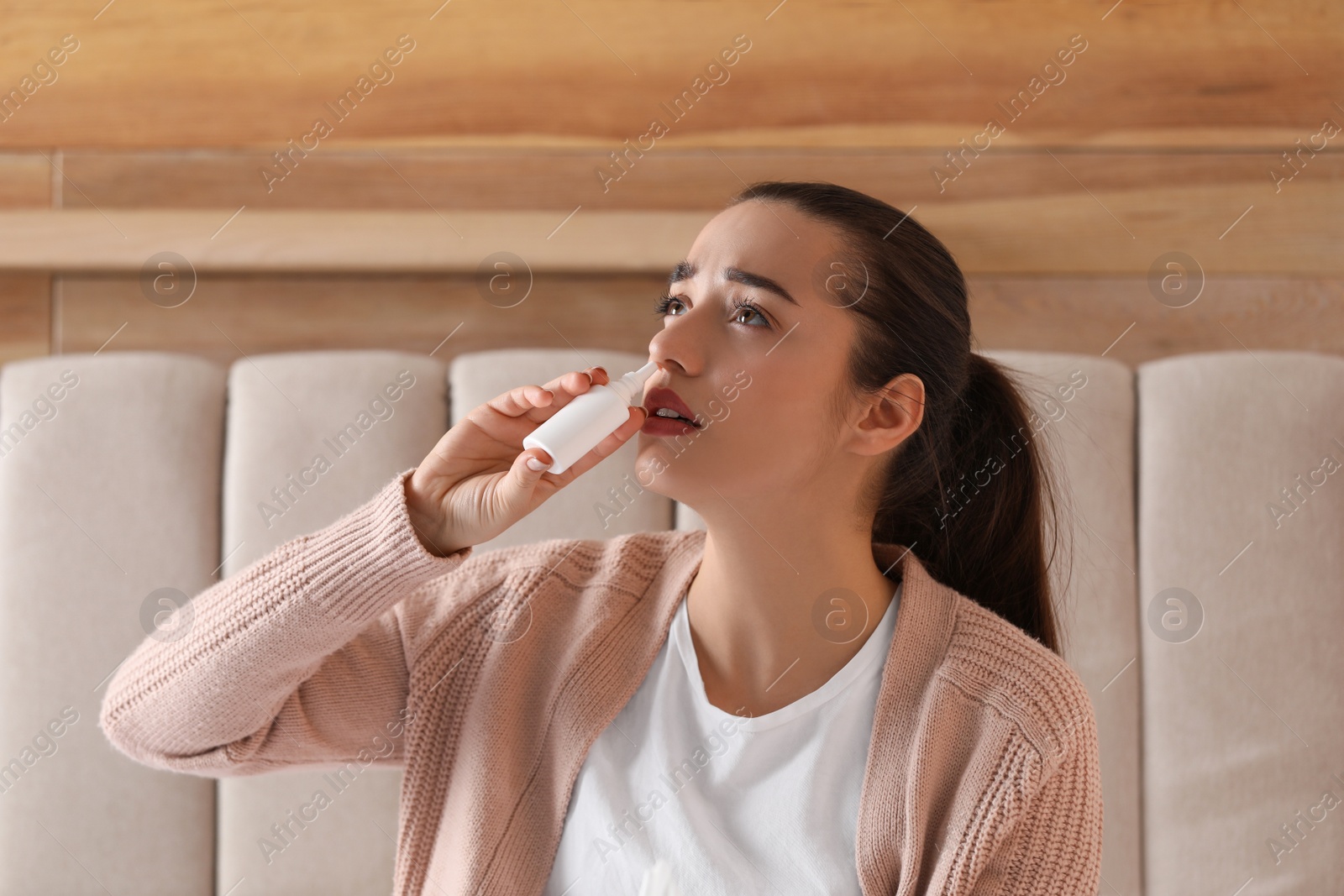 Photo of Sick young woman using nasal spray in bed at home