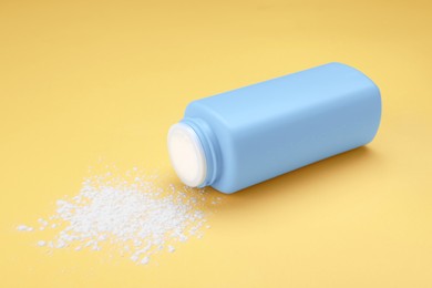 Bottle and scattered dusting powder on yellow background. Baby cosmetic product