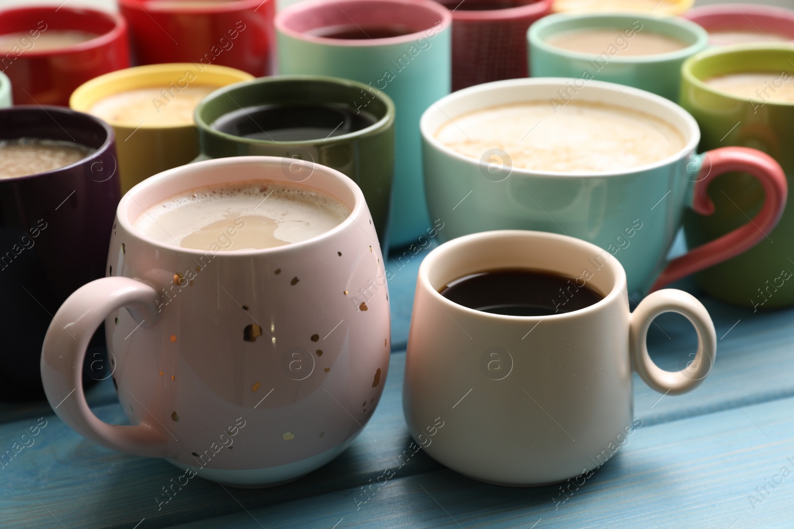 Photo of Many cups of different coffee drinks on light blue wooden table