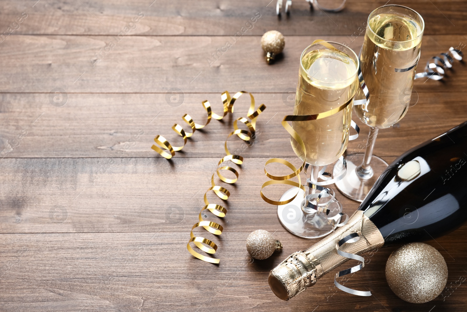 Photo of Glasses and bottle of champagne, serpentine streamers with Christmas balls on wooden table. Space for text