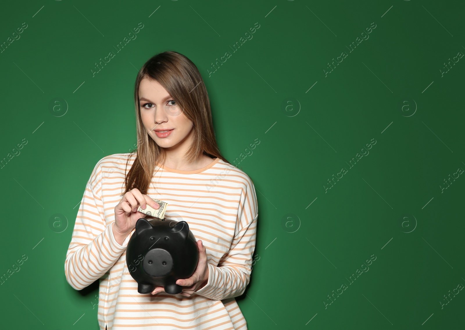 Photo of Young woman putting money into piggy bank on color background. Space for text