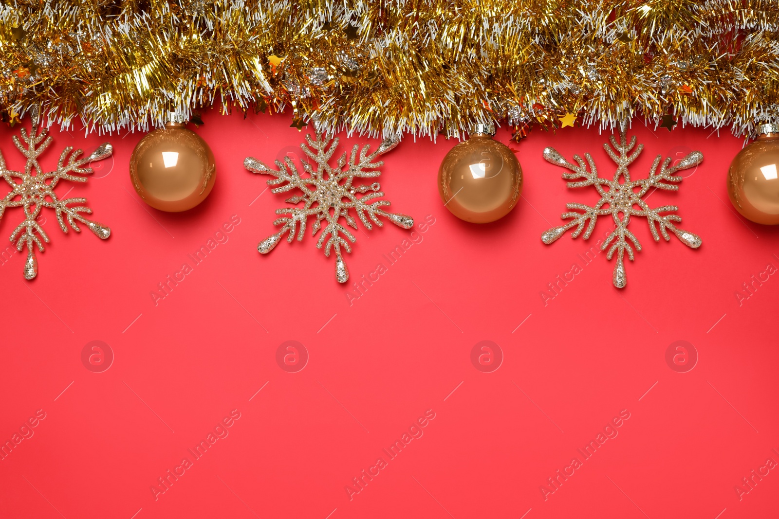 Photo of Golden tinsel with Christmas decor on red background, flat lay. Space for text