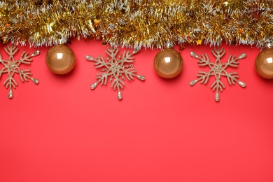 Golden tinsel with Christmas decor on red background, flat lay. Space for text