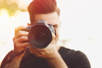 Image of Photographer taking picture with professional camera outdoors , focus on lens