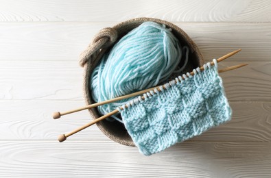 Photo of Soft turquoise yarn, knitting and needles on white wooden table, top view