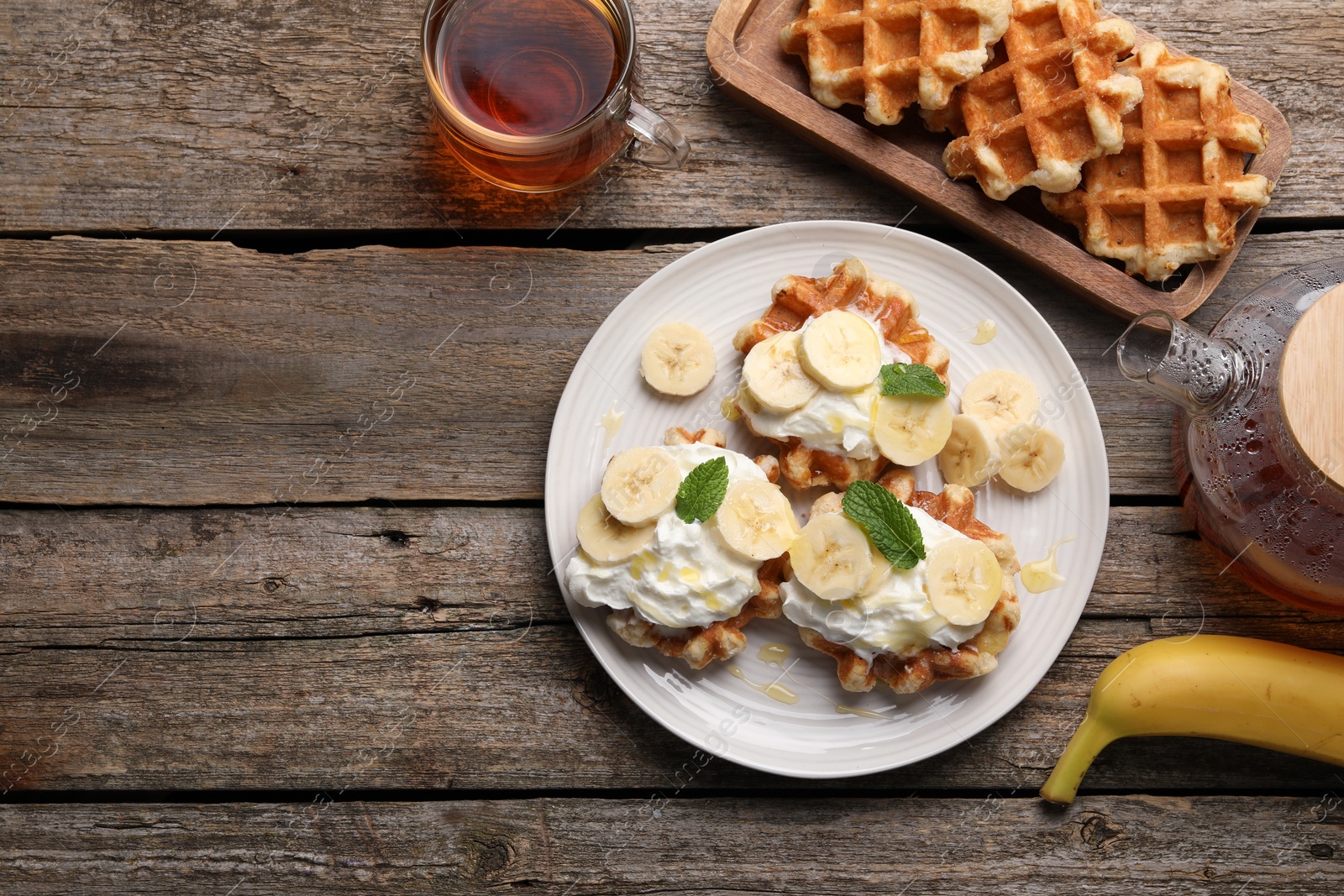 Photo of Delicious Belgian waffles with banana and whipped cream served on wooden table, flat lay. Space for text