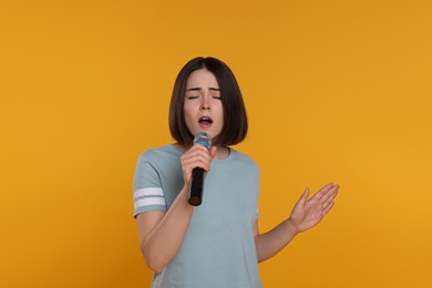 Photo of Beautiful young woman with microphone singing on yellow background