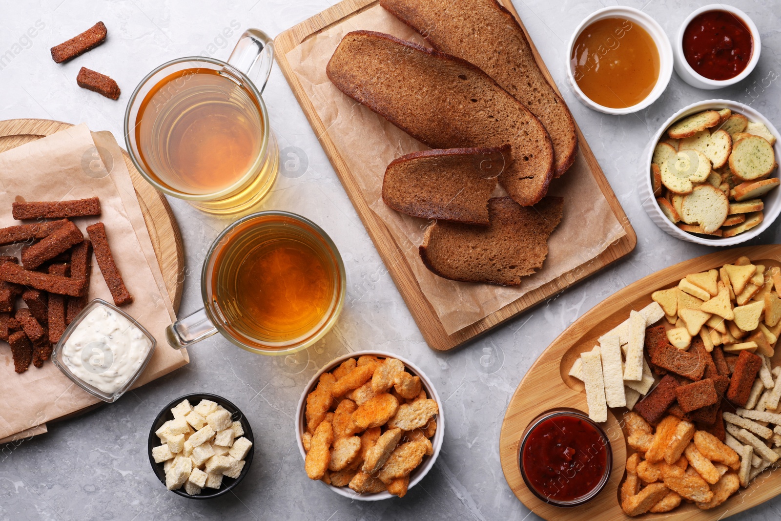 Photo of Different crispy rusks, beer and dip sauces on light marble table, flat lay