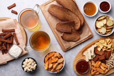 Different crispy rusks, beer and dip sauces on light marble table, flat lay