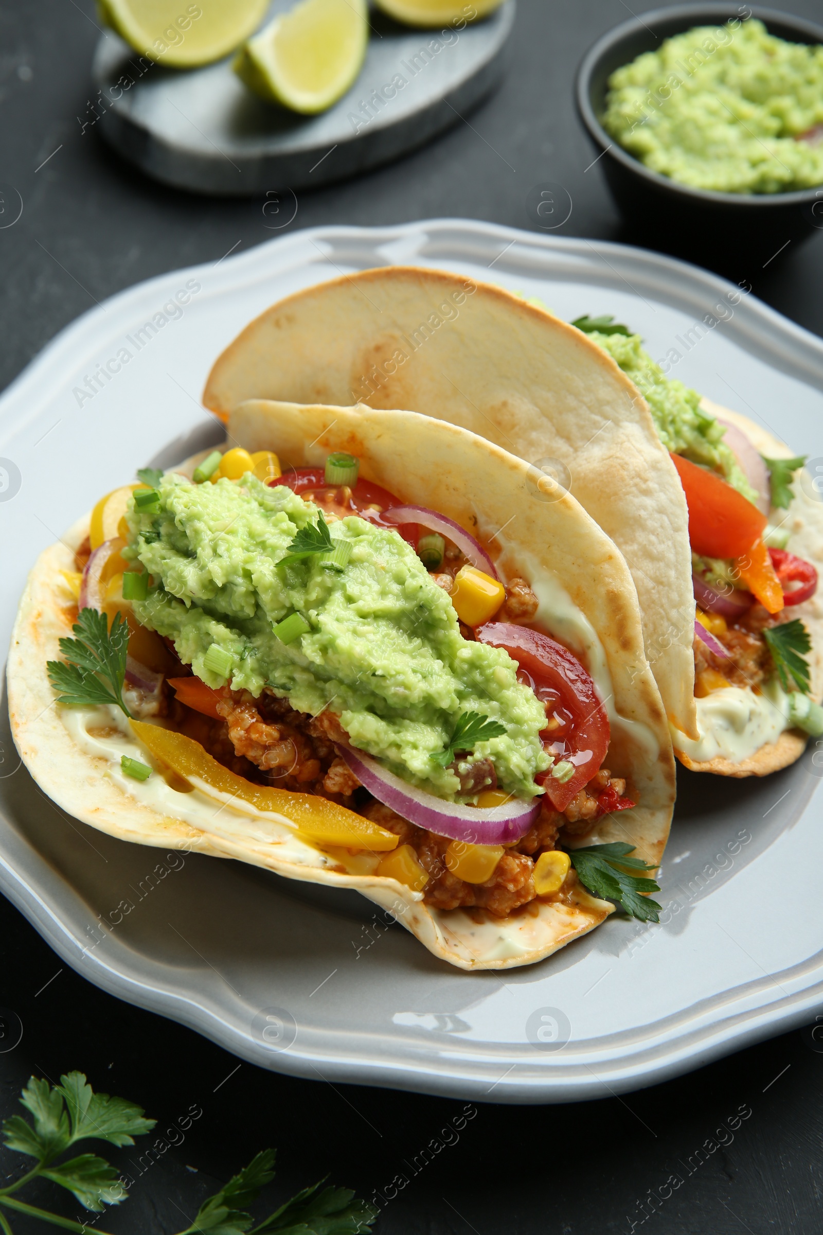 Photo of Delicious tacos with guacamole, meat and vegetables on black table, closeup