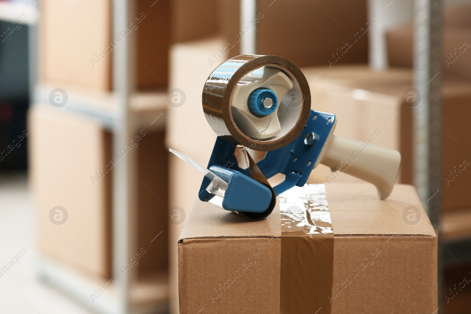 Photo of Adhesive tape dispenser on cardboard box indoors. Space for text