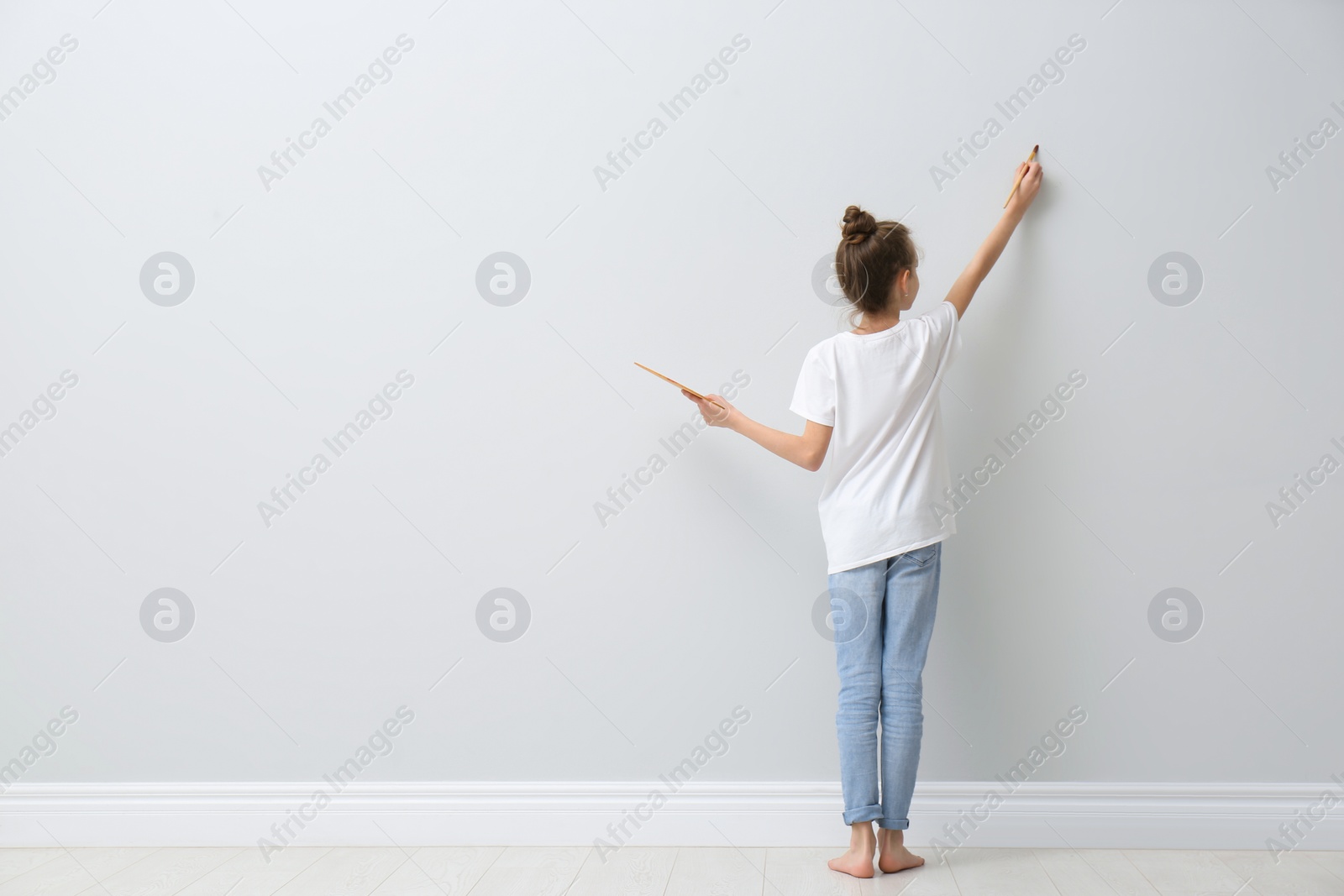 Photo of Little girl painting on light wall indoors, back view. Space for text