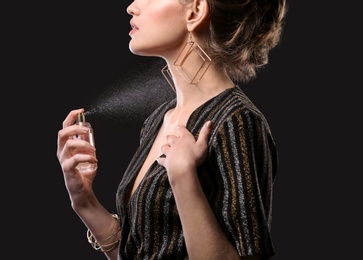Beautiful young woman with bottle of perfume on black background
