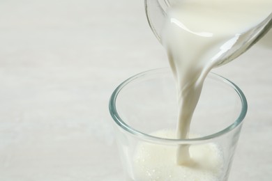 Photo of Pouring milk into glass on white table, closeup. Space for text