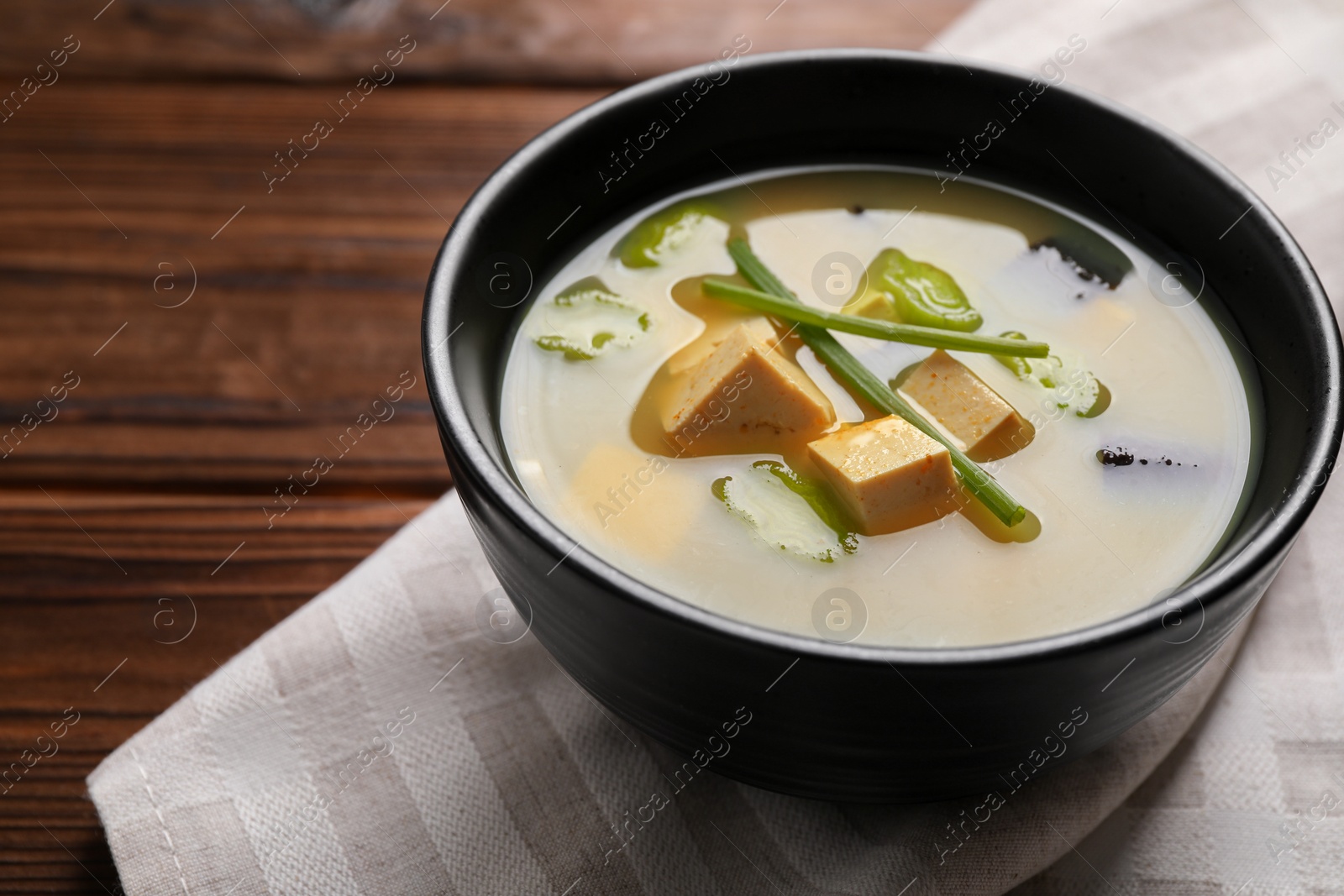 Photo of Bowl of delicious miso soup with tofu on wooden table, closeup. Space for text