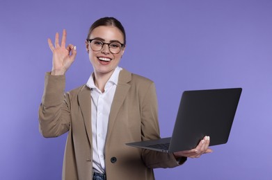 Photo of Happy woman in glasses with laptop showing okay gesture on violet background