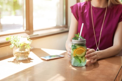 Young woman with mason jar of tasty natural lemonade in cafe, closeup. Detox drink