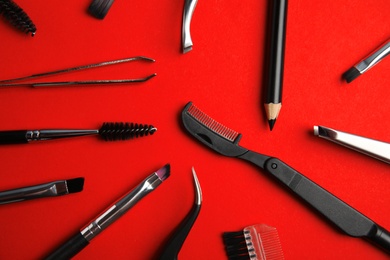 Set of professional eyebrow tools on red background, flat lay