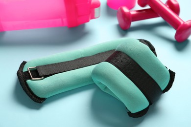 Photo of Turquoise weighting agents, dumbbells and shaker on light blue background
