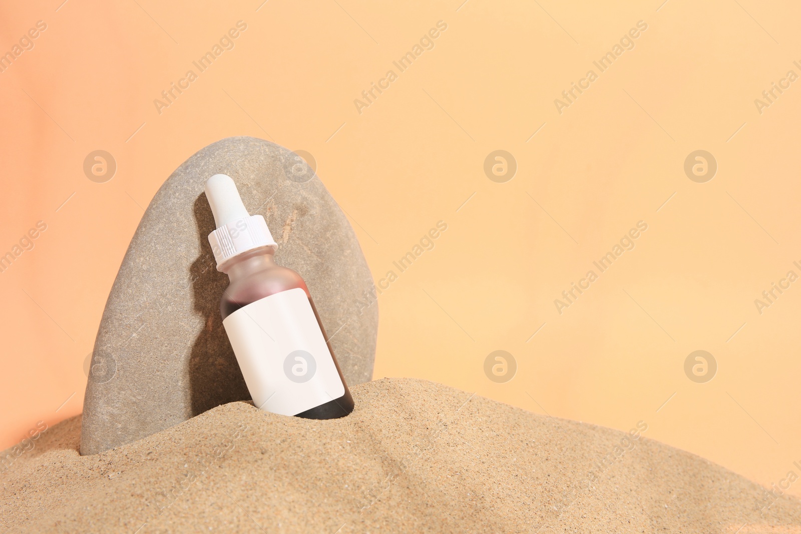 Photo of Bottle with serum and stone on sand against orange background, space for text. Cosmetic product