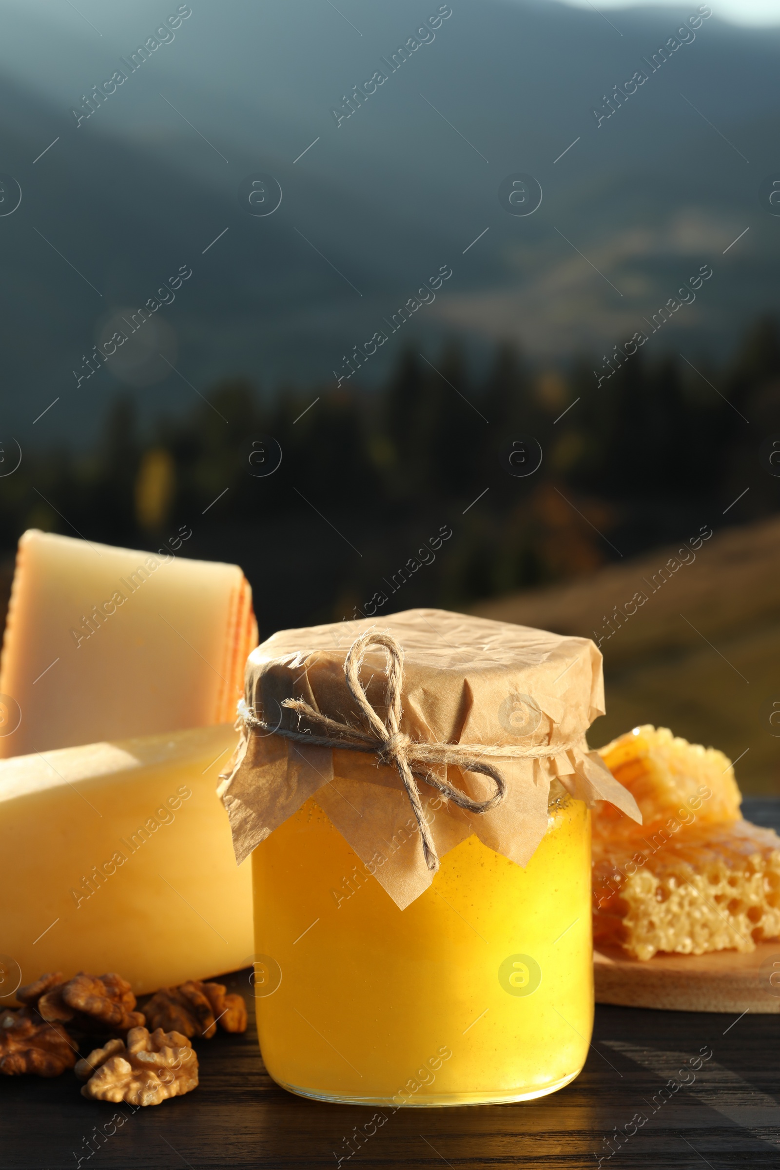 Photo of Fresh aromatic honey, combs, cheese and nuts on wooden table against mountain landscape