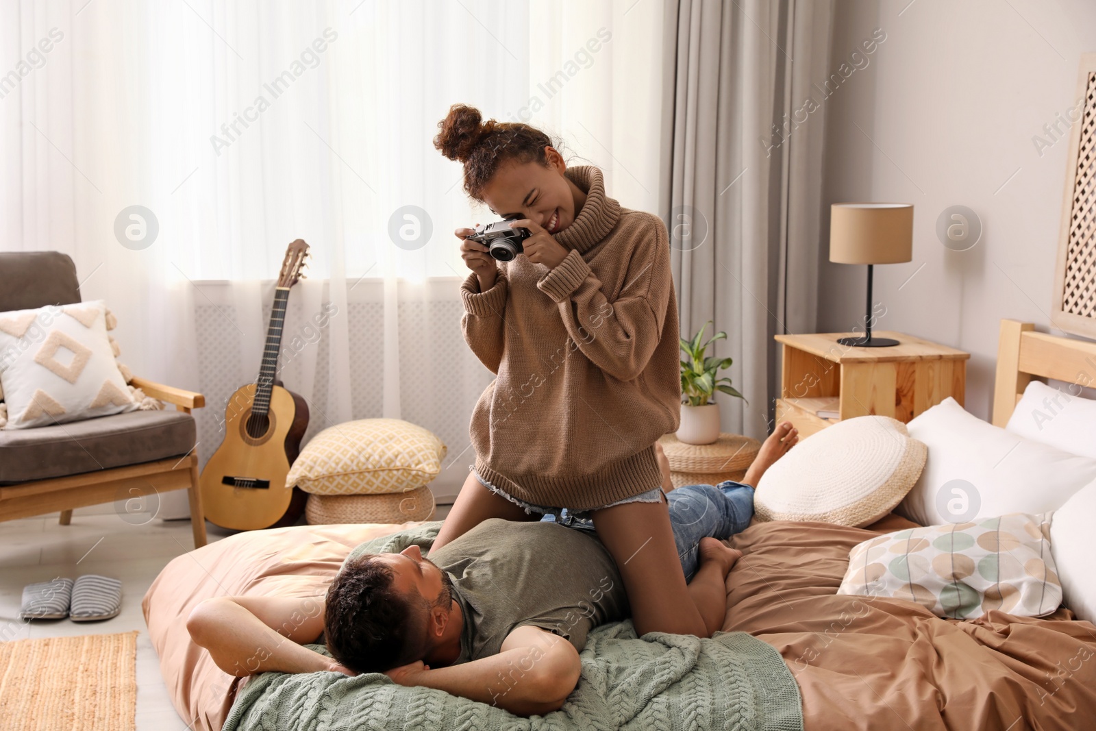 Photo of Beautiful African-American woman taking picture of her boyfriend on bed at home