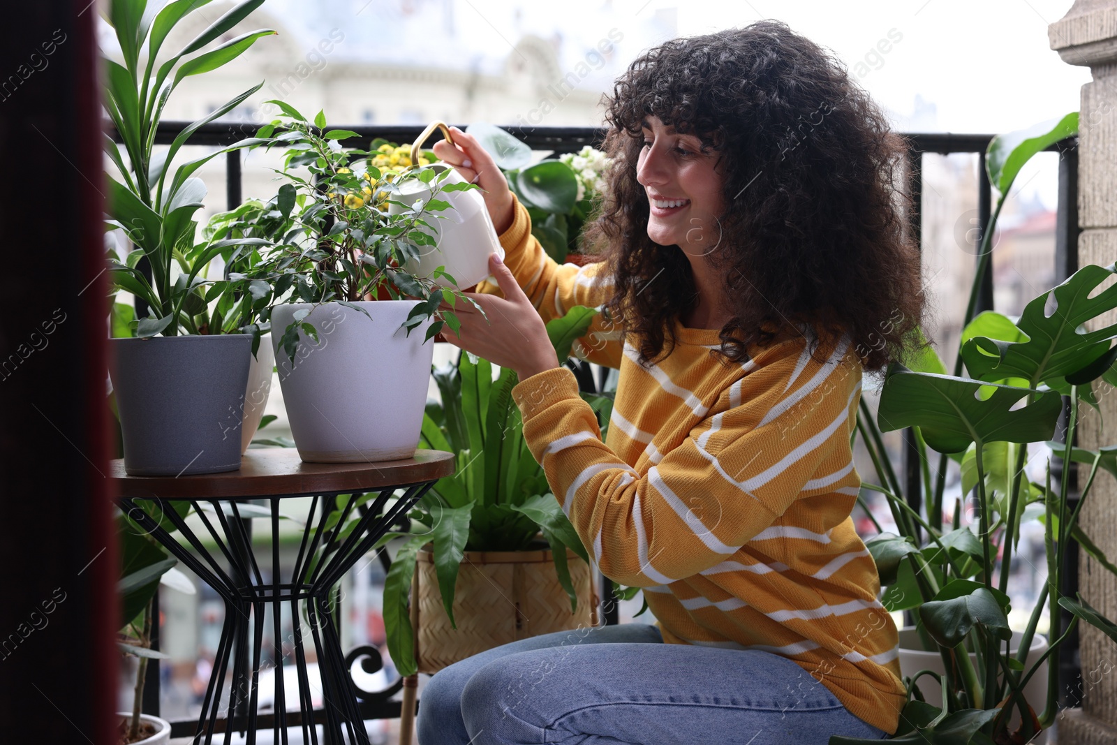 Photo of Beautiful young woman watering green houseplants on balcony