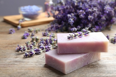 Photo of Handmade soap bars with lavender flowers on brown wooden table, closeup. Space for text