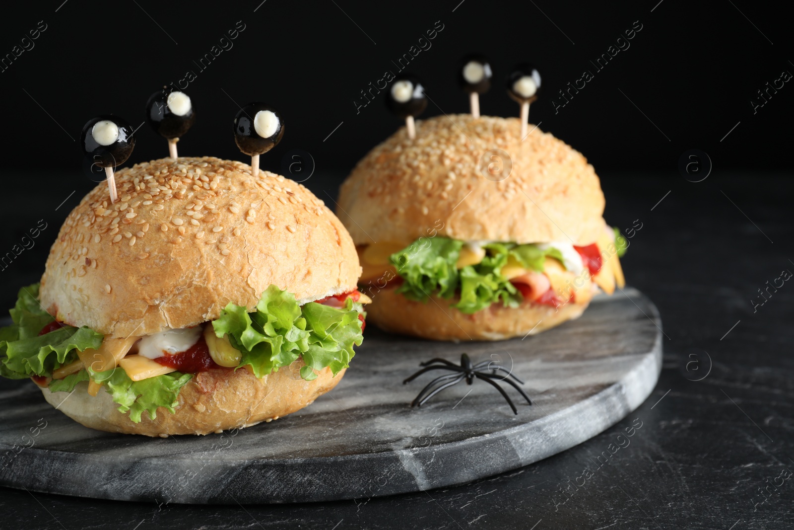 Photo of Cute monster burgers served on black table. Halloween party food