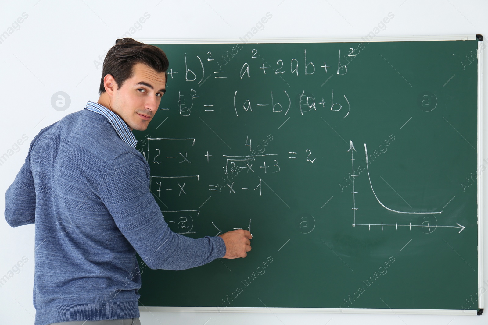 Photo of Young teacher writing math formulas on chalkboard in classroom