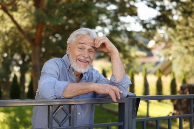 Photo of Portrait of happy senior neighbour leaning on fence outdoors