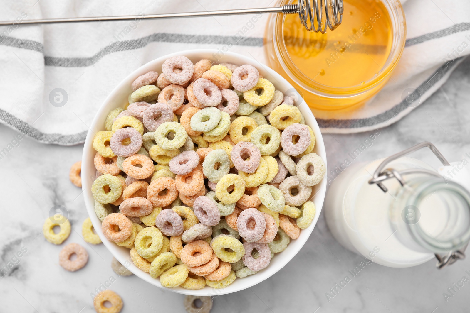 Photo of Tasty cereal rings in bowl, milk and honey on white marble table, flat lay