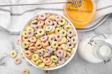 Tasty cereal rings in bowl, milk and honey on white marble table, flat lay