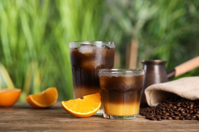 Photo of Tasty refreshing drink with coffee and orange juice on wooden table against blurred background