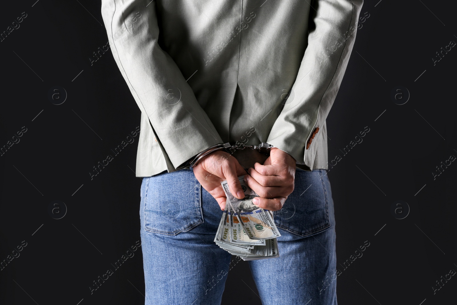 Photo of Man in handcuffs holding bribe money on black background, closeup