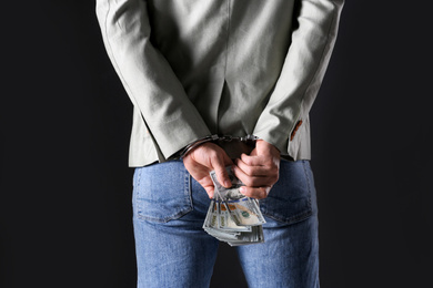 Photo of Man in handcuffs holding bribe money on black background, closeup