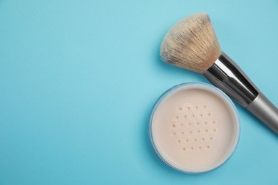 Loose face powder and brush on light blue background, flat lay. Space for text