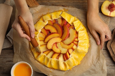 Woman making peach pie at wooden table, top view